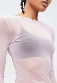 Haut à manches longues rose clair en tissu résille transparent, avec un col arrondi et une superposition d'un vêtement gris en dessous.