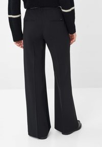Pantalons larges noirs avec une texture lisse, dotés de deux poches arrière et d'une coupe ajustée, stylés avec une taille haute.