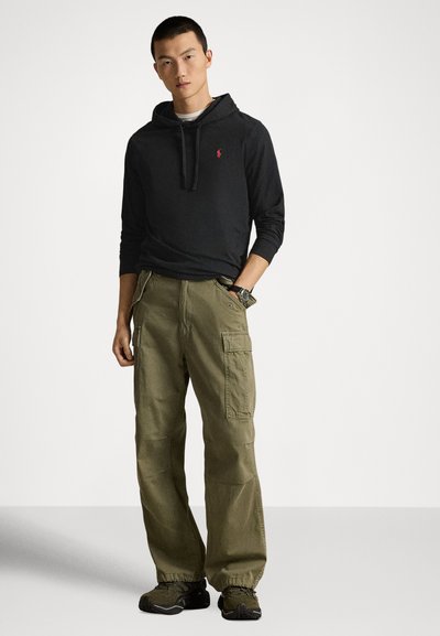Svart huvtröja med liten röd logotyp, kombinerad med olivfärgade cargobyxor med sidofickor och åtdragna benslut, bärs med mörka sneakers.