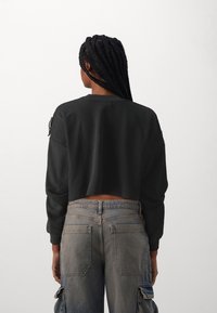 Felpa nera corta con maniche lunghe, realizzata in cotone. Abbinata a jeans cargo blu sbiaditi con molteplici tasche e una vestibilità comoda.