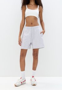 Pantaloni shorts in cotone grigio chiaro con cintura elastica e cordino, dotati di tasche laterali. Abbinati a un top corto bianco e sneakers.