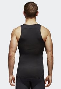 Haut de sport noir sans manches avec une coupe ajustée, une texture lisse et un col montant, avec des coutures renforcées le long des coutures.