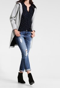 Light gray hooded coat, black polka dot blouse, distressed blue jeans, black ankle boots. Casual, modern ensemble with layered textures.