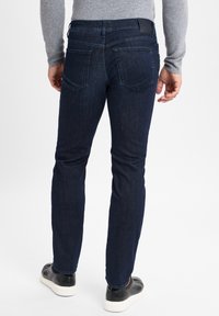 Donkerblauwe denim jeans met een slim fit, voorzien van twee achterzakken en een leren tailleband label, gecombineerd met zwarte schoenen met een gladde zool.