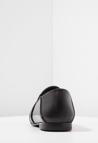 Chaussure en cuir noir à texture lisse, talon arrondi, talon bas et design minimaliste. Aucun élément visible de quincaillerie ou motif.