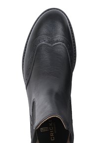 Bottine en cuir noir avec des détails en brogue, finition lisse, côtés élastiques et semelle texturée. Accents cousus le long des bords.