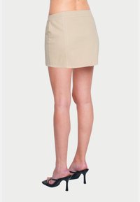 Mini gonna beige in misto cotone, con dettagli di cucitura visibili. Abbinata a sandali neri con tacco alto.
