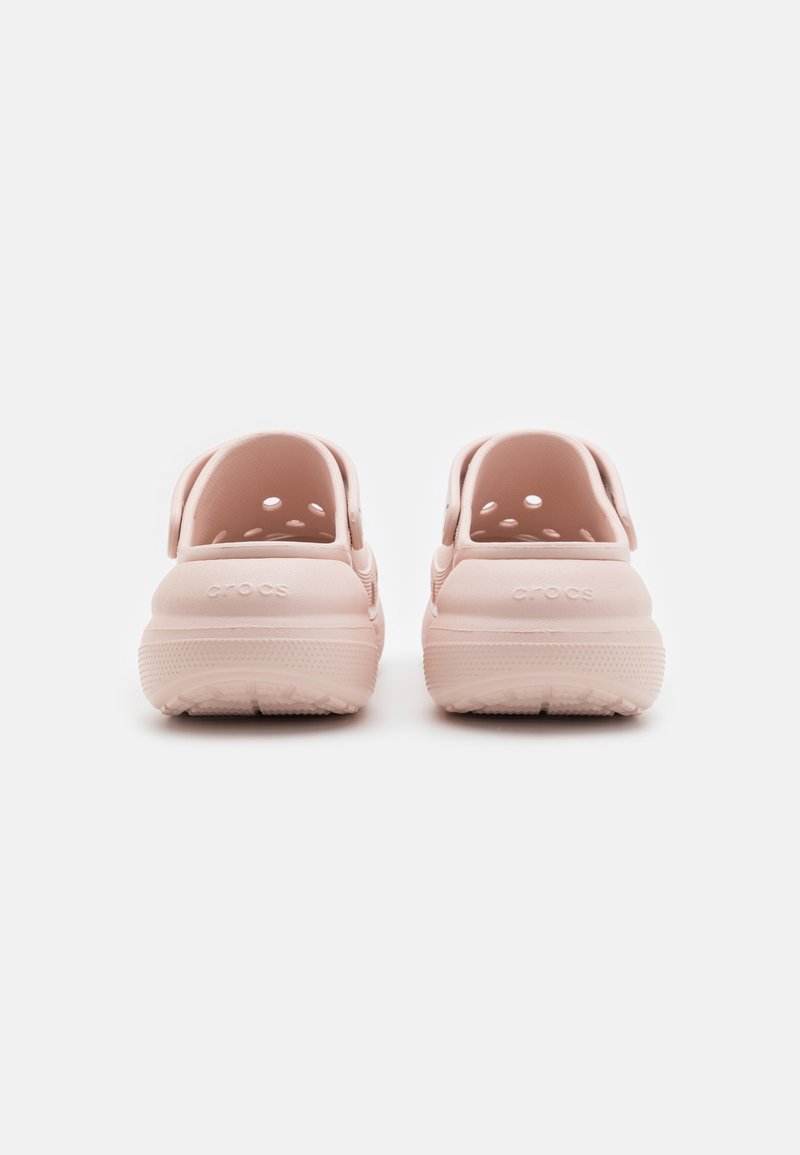 Zuecos Crocs de color rosa claro con orificios de ventilación y correas traseras. Material plástico suave con una suela texturada para agarre y soporte.