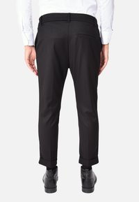 Pantaloni neri su misura con una vestibilità slim, caratterizzati da un orlo arrotolato, tasche laterali e una texture liscia, abbinati a calzature nere.