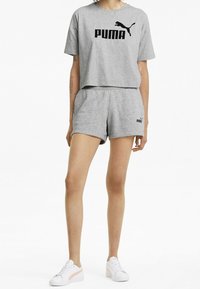 Harmaa puuvillainen crop-t-paita mustalla "PUMA"-logolla, yhdistettynä matching harmaisiin shortsit logoyksityiskohdalla. Yllä valkoiset lenkkitossut.