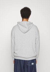 Grå hettegenser med myk tekstur, avslappet passform og ribbestrikkede mansjetter. Brukt sammen med løse denimshorts med synlig merkelapp.