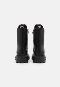 Bottines en cuir noir avec une semelle en caoutchouc épaisse, fermeture zippée à l'arrière et finition lisse, ornées d'accents en métal doré.