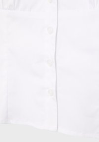Gros plan sur un tissu blanc avec une rangée verticale de petits boutons ronds et une couture cousue sur le côté.