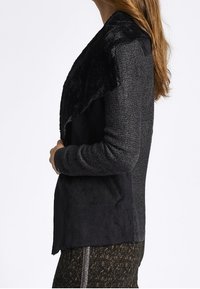Black jacket with textured gray fabric, featuring a soft faux fur collar and side pockets. Open front design with a relaxed fit.