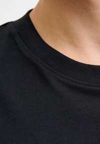 Must must-särk mustast puuvillast, millel on soonikuga ümar kaelus. Sile sile tekstuur, lähedalt vaade kangale ja õmblusdetailidele.