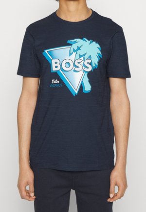 Man wearing a navy blue T-shirt with a blue palm tree and triangle graphic and the words "BOSS Enter Vacancy" printed on front.