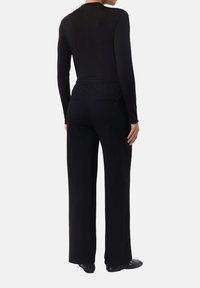 Body nero a maniche lunghe con design aderente, abbinato a pantaloni neri a vita alta, larghi, con tasche laterali e gamba dritta.