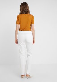 Hnědé tričko s krátkým rukávem zastrčené do bílých slim-fit kalhot se zadními kapsami. Oblečení doplňují světlé lodičky na podpatku.