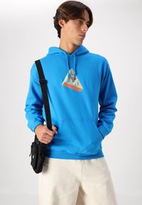 Blue hoodie in cotton blend with front pocket and drawstring hood, featuring a triangular graphic design in orange and yellow. Black crossbody bag.