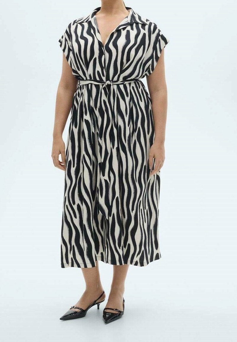 Femme portant une robe midi à rayures zébrées noires et blanches, manches courtes et ceinture nouée à la taille, associée à des escarpins noirs à bouts pointus et bride arrière.