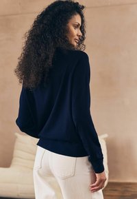 Mörkblå sweatshirt med en avslappnad passform, ribbade ärmslut och nederkant, tillsammans med ljusa jeans. Mjuk textur, enkel design utan synliga mönster.