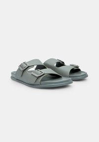 Sandale din plastic verde cu două catarame ajustabile, design cu vârf deschis și talpă texturată pentru aderență. Formă simplă, minimalistă.
