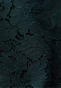 Tissu en dentelle vert foncé avec broderie florale en relief et détails en maille créant un motif texturé et complexe.