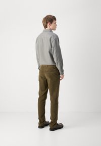 Chemise en flanelle grise avec col, associée à un pantalon en velours côtelé vert olive. Détails notables incluent des boutons et une poche arrière sur le pantalon.