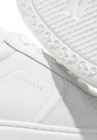 Hvite lær sneakers med teksturerte semskede detaljer, med en glatt finish, perforeringer og en gummisåle preget med et sirkulært mønster.