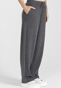 Szare, szerokie spodnie dresowe z miękkiego materiału z elastycznym pasem i sznurkiem do regulacji. Posiadają boczne kieszenie oraz dekoracyjne przeszycia wzdłuż szwów.