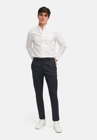 Witte overhemd met knopen, donkere geruite broek en witte sneakers. Slim fit met stevig stof in een moderne snit, voorzien van subtiele ruitpatronen.