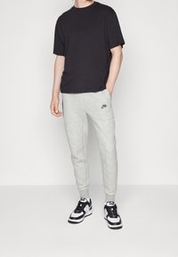 Svart bomulls-T-shirt, grå mjukisbyxor med logga och svartvita sneakers. Avslappnad passform, minimalistisk design, slät textur.