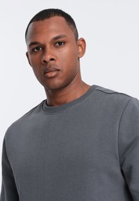 Sweatshirt gris à col rond, avec des poignets côtelés et des accents d'épaule. Texture douce avec un design minimaliste.