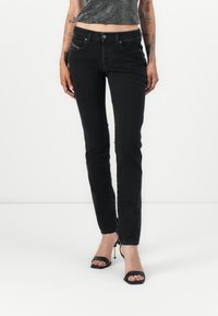 Black denim skinny jeans with a mid-rise waist, five-pocket design, and subtle red stitching. Smooth texture and fitted cut.