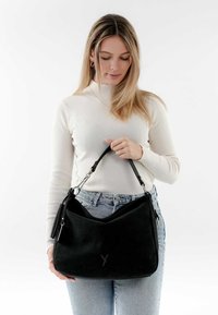 Schwarze Wildleder-Handtasche mit geschwungener Form, doppelten Griffen und silbernen Beschlägen. Mit einer seitlichen Quaste und geprägt Logo auf der Vorderseite.