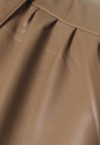 Braunes Ledergewebe mit glatter Textur und leichtem Glanz, mit Falten, die Tiefe und visuelles Interesse schaffen.