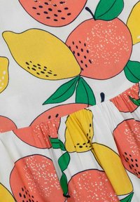 Ein Stoff mit einem Muster aus orangefarbenen und gelben Zitronen auf einem cremfarbenen Hintergrund, mit lebhaften Farben, schwarzen Konturen und gerafften Details.