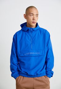 Kék, könnyű pulóverdzseki elülső zsebbel és állítható kapucnival. Rugalmas mandzsettákkal és derékkal rendelkezik, a zsebén a "JORDAN" logóval.