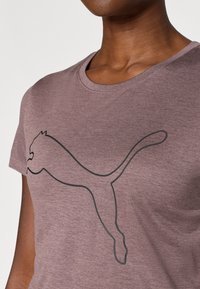 T-shirt z krótkim rękawem w kolorze mauve, wykonany z miękkiego materiału, z grafiką czarnego logo Puma w eleganckim designie i gładkiej fakturze.