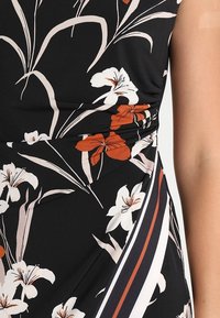 Vestido negro con estampados florales en blanco y naranja, de tejido texturizado, cintura fruncida y rayas diagonales en rojo y blanco.