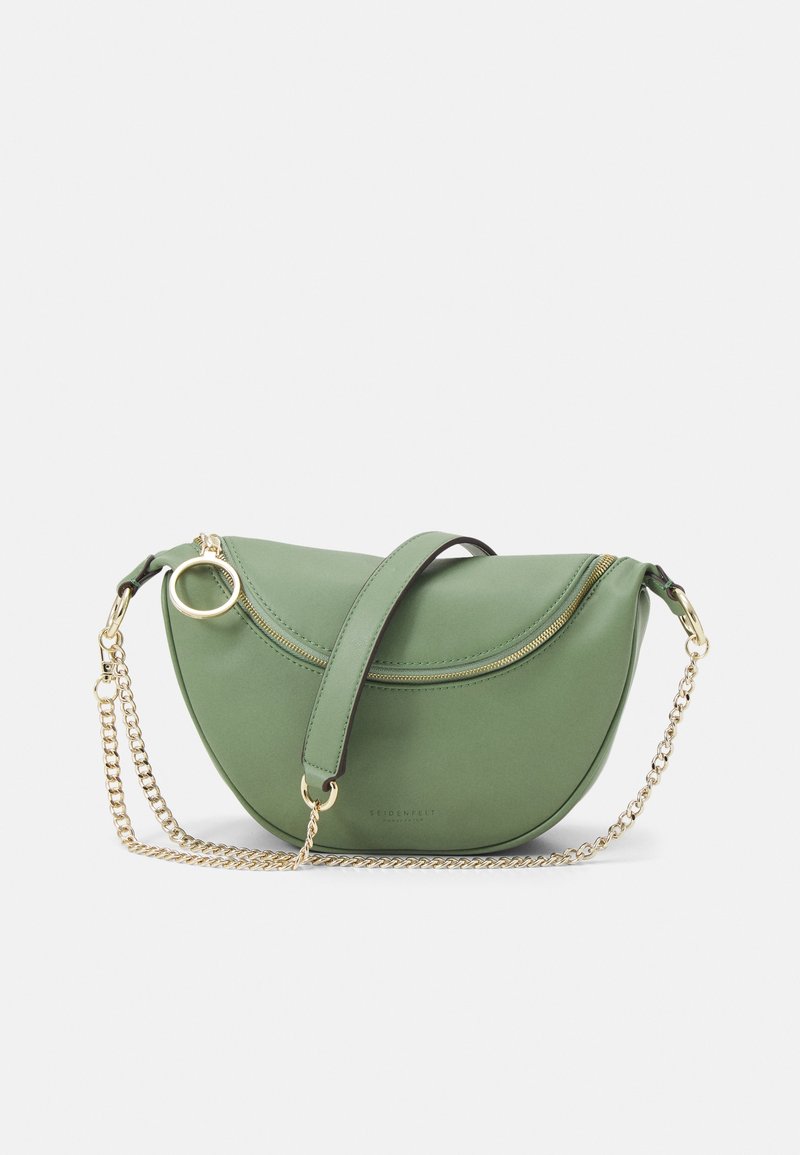 Sac en cuir vert avec un design courbé, bandoulière chaîne dorée, fermeture éclair sur le dessus et un détail circulaire en métal. Texture lisse, branding minimal.
