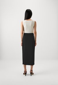 Top bianco a coste senza maniche abbinato a una gonna nera al ginocchio. La gonna ha una texture liscia e un accento a fiocco in vita. Tacchi neri.