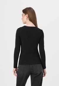 Svart langermet topp med en tettsittende design, teksturert med glitrende detaljer. Rund utrigning, glatt stoff, kombinert med mørkegrå jeans.