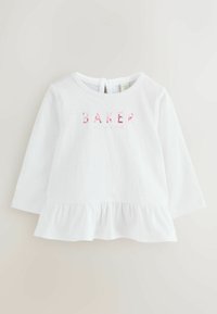 Balta garu piedurkņu krekls ar frillēm apakšmalā un ziedu raksta "BAKER" tekstu priekšpusē. Mīksta kokvilnas audums, apaļa kakla izgriezums un pogas aizdare aizmugurē.