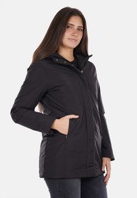 Giacca nera impermeabile con zip frontale, colletto alto e due tasche laterali. Presenta un design semplice e una texture liscia.