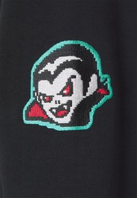 Tissu noir avec un motif de tête de vampire en pixels. Le design met en avant des yeux rouges, un visage blanc et des accents verts autour de la bordure.