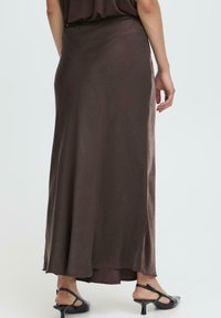 Ilga ruda satino sijonas su lygiu paviršiumi, turintis subtilų spindesį ir grindų ilgį, derinamas su juodais aukštakulniais sandalais.