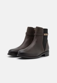 Bottines en cuir marron avec une fermeture éclair sur le côté, des panneaux élastiques et un accent en métal doré. Semelle plate et design à orteil arrondi.