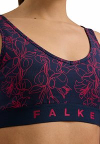 Navy sports bra with pink floral pattern, scoop neckline, and wide elastic band featuring "FALKE" in pink lettering. Soft, stretchy fabric.