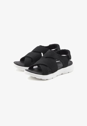 Schwarze geflochtene Sandalen mit einem Kreuzgurt-Design, ausgestattet mit einem strukturierten Obermaterial und einer weißen Gummisohle. Offene Zehenform für Atmungsaktivität.